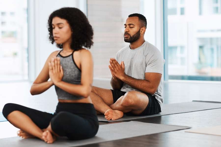 Un homme et une femme pratiquent la méditation assis, une étape clé dans la progression en yoga.