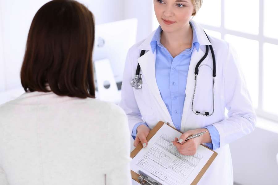 Une femme médecin en blouse blanche avec un stéthoscope discute avec une patiente dans un cabinet médical lumineux.